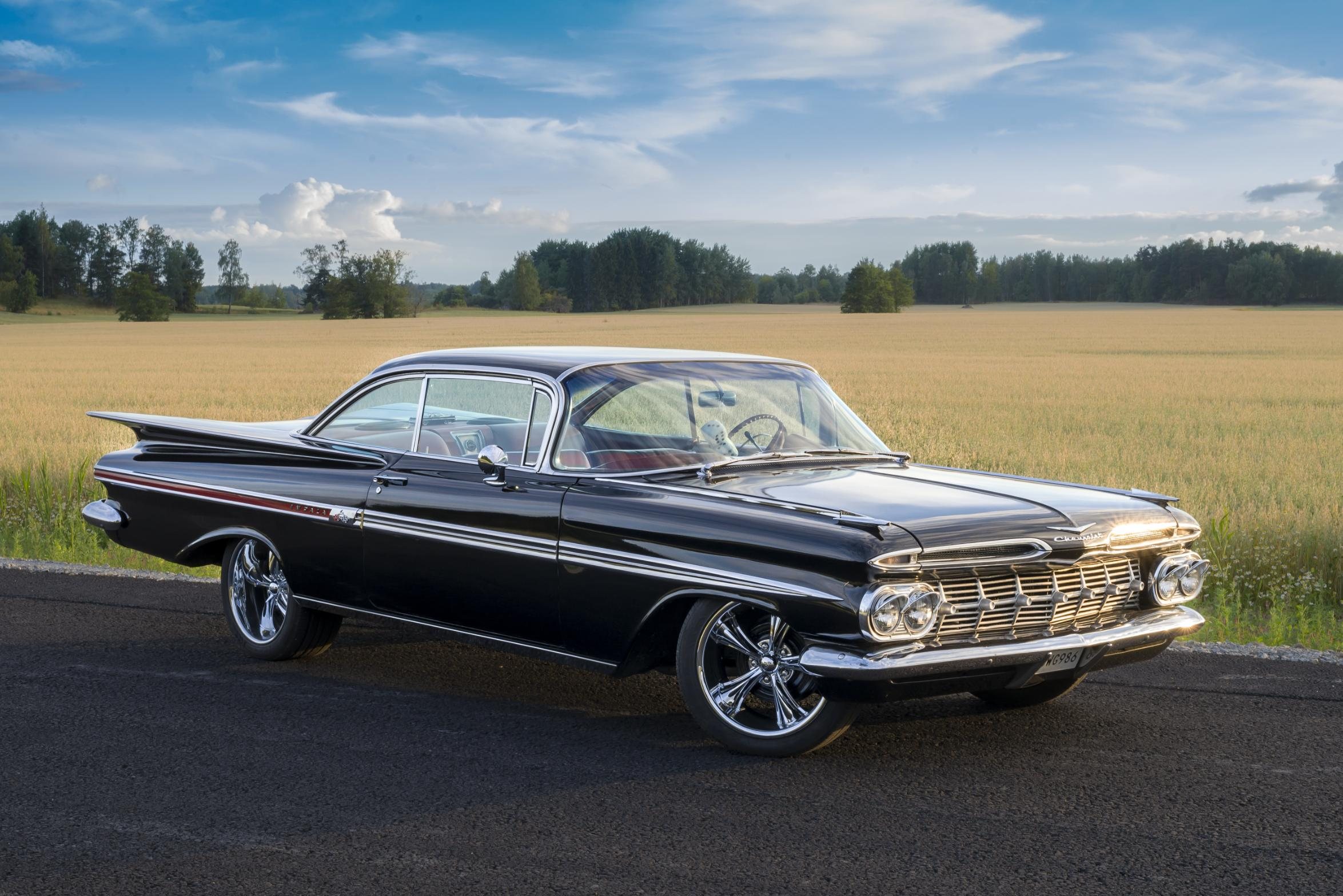 Svart Chevrolet Impala 1959 med kromfälgar framför ett gyllene fält i kvällsljus